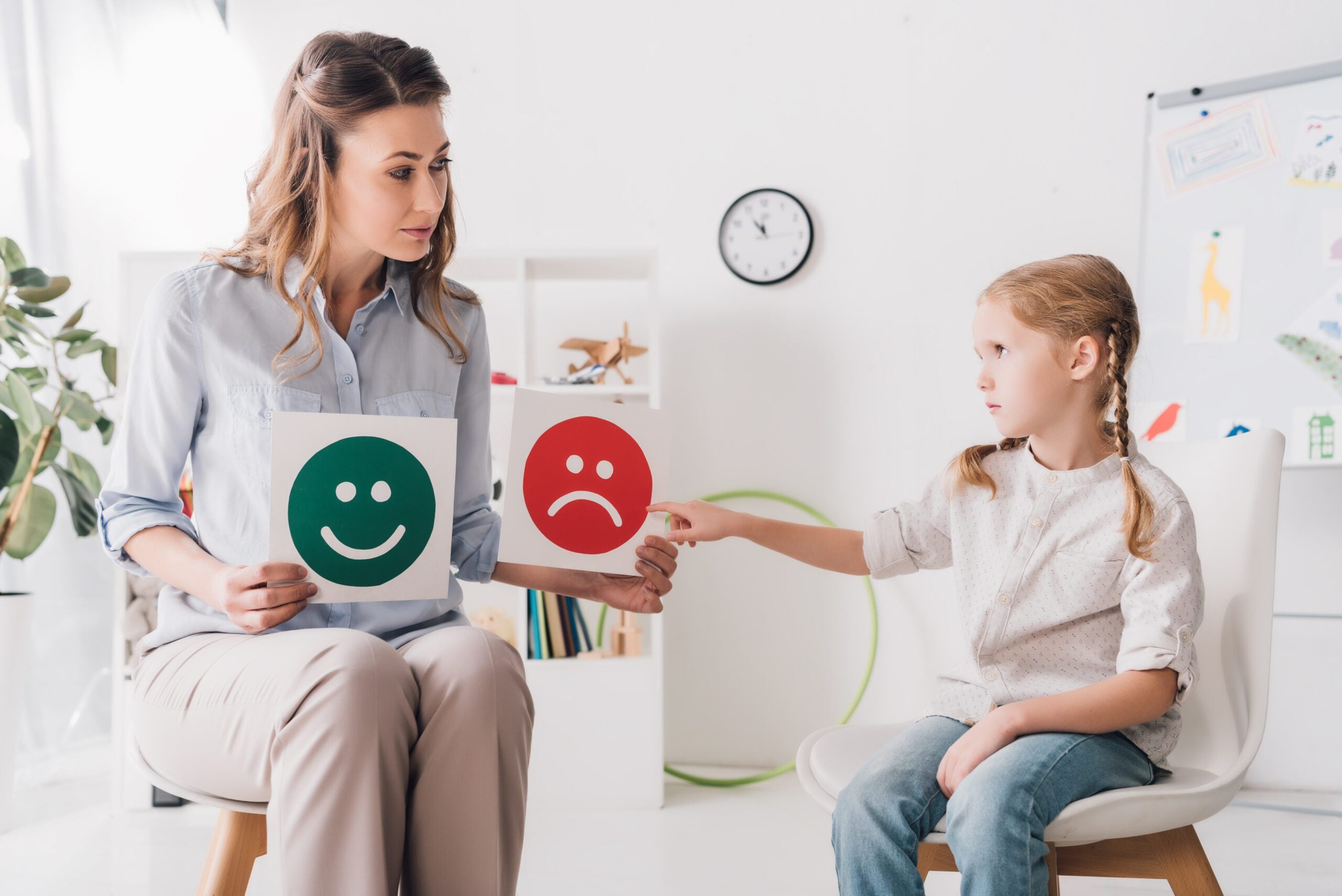 Child psychologist showing happy and sad emotion cards — emotion recognition in autism therapy