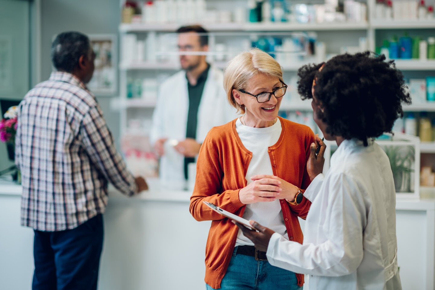 Pharmacist at the script counter handing a medication to a patient — the moment where a medical ID recommendation lands