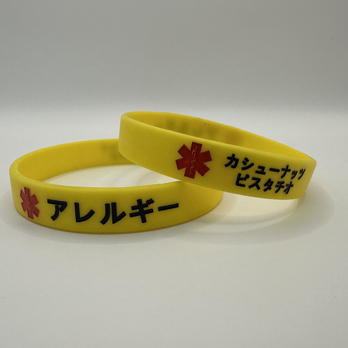 Two yellow Mediband silicone bracelets engraved in Japanese — アレルギー (allergy) and カシューナッツ ピスタチオ (cashew nuts, pistachio) — for travellers in Japan with tree-nut anaphylaxis
